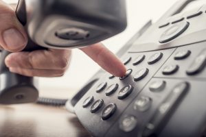 Closeup of male hand holding telephone receiver while dialing a telephone number to make a call using a black landline phone. With retro filter effect.